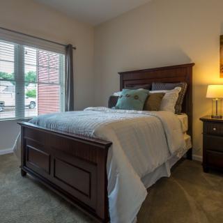A cozy bedroom with a wooden bed, nightstand, and a lit lamp.