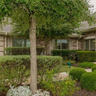 A well-maintained residential garden with neatly trimmed bushes and a tree in front of a house.