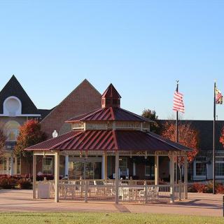 A gazebo in a park setting with flags and buildings in the background, under a clear blue sky.