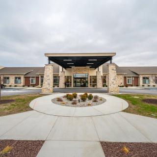 A modern building entrance with a circular driveway and landscaped surroundings under a cloudy sky.