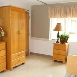 A cozy room featuring wooden furniture, including a wardrobe and nightstand with a lamp near a window.