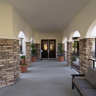 A covered entrance corridor with stone pillars, potted plants, and a bench.