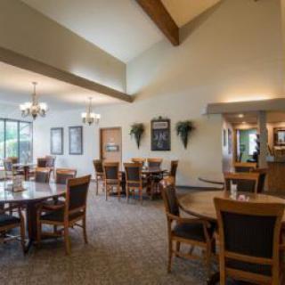A cozy restaurant dining area with wooden tables and chairs, soft lighting, and wall decorations.