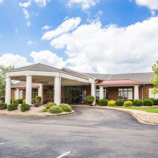 A welcoming hotel entrance surrounded by well-maintained landscaping under a bright, cloudy sky.