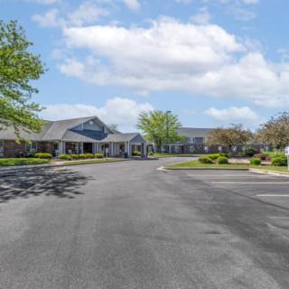 A view of a large building with a spacious driveway surrounded by trees under a partly cloudy sky.