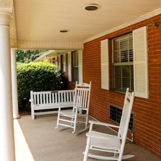 A serene porch featuring white rocking chairs and a bench, perfect for relaxation.