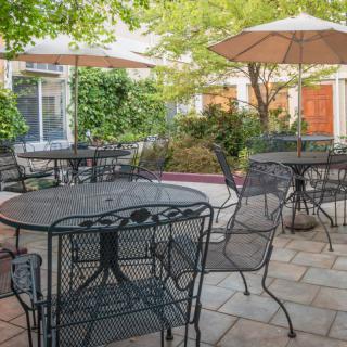 Cozy outdoor patio with iron tables, chairs, and umbrellas surrounded by greenery.