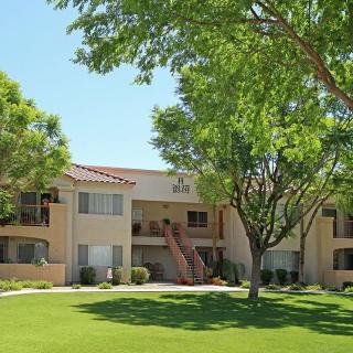 A sunny view of an apartment building surrounded by trees and a grassy lawn.
