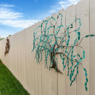 Decorative metal tree art mounted on a wooden fence.
