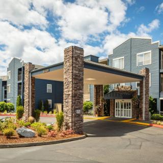 A modern hotel building with a welcoming entrance and landscaped surroundings under a cloudy sky.