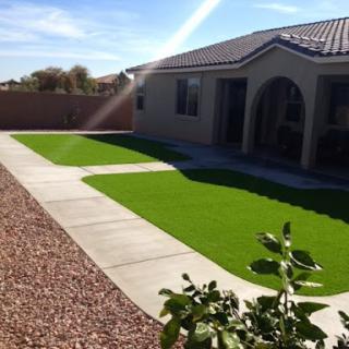 A well-maintained yard featuring artificial grass and a paved pathway leading to the house.