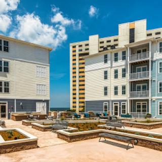 A view of a modern apartment complex featuring two buildings and a landscaped courtyard under a bright blue sky.