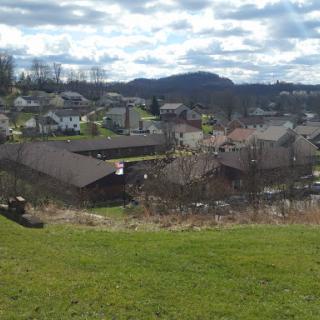 A scenic view of a town nestled among the hills, with a mix of residential homes and greenery under a cloudy sky.