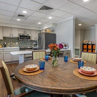 A modern kitchen and dining area featuring a round wooden table with colorful place settings and a vase of flowers.
