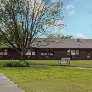 A single-story building with a tree and bench in the foreground.