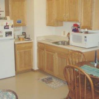 A compact kitchen with wooden cabinets, a microwave on the counter, and a small dining area.