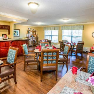 A cozy dining room with wooden floors, featuring several tables and chairs arranged neatly, decorated in a warm and inviting style.