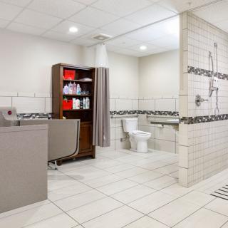 A spacious, modern bathroom designed for accessibility with a tiled floor and walls, featuring a sink, toilet, shower area, and storage shelves.