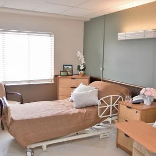 A well-lit and cozy hospital patient room, featuring a bed, bedside table, and natural light from the window.