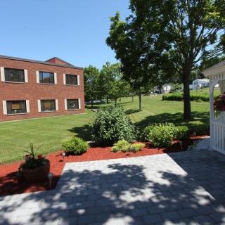 A landscaped garden area with a red-brick building in the background under a clear blue sky.