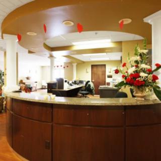A well-lit reception area with a wooden desk and floral decorations.