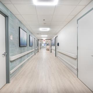 A bright and clean corridor in a modern hospital, featuring multiple doors and wall art.