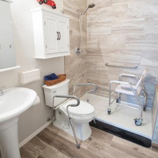An accessible bathroom featuring a shower, toilet, and sink, equipped with safety grab bars and mobility aids.