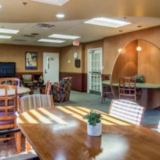 A well-lit communal living space with tables, chairs, and decorative plants.