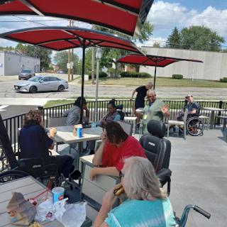 A group of people enjoying a casual meal outside at a restaurant on a sunny day.