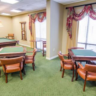 A cozy room with tables and chairs set up for gatherings, featuring green carpeting and natural light.