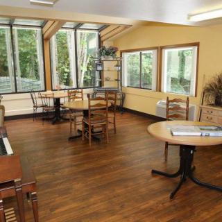 A bright room with wooden floors and several tables and chairs, illuminated by natural light through large windows.