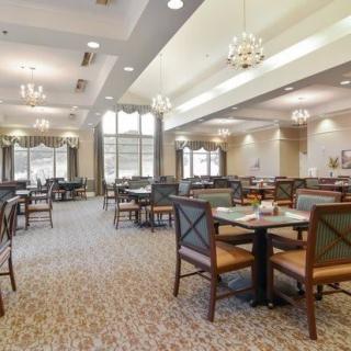 A spacious dining area with elegant chandeliers, featuring multiple tables and chairs on a patterned carpet.