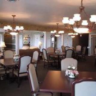 An elegantly furnished dining room with multiple tables and chairs, decorated with chandeliers and flowers.