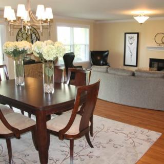 A stylish open-plan dining and living area featuring elegant furniture, a dining table with flowers, and a cozy sofa setup.