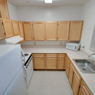 A small kitchen featuring wooden cabinets, a countertop with a sink, a stove, a refrigerator, and a microwave oven.