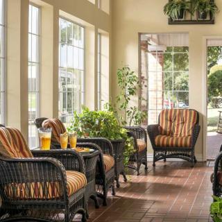 A cozy sunroom with wicker furniture, plants, and abundant natural light streaming through large windows.