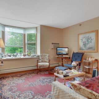 A cozy living room with classic decor, featuring a large window, patterned carpet, and comfortable seating.