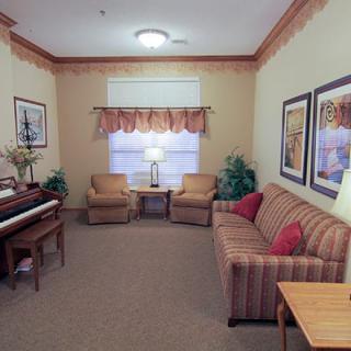 A cozy living room featuring a striped sofa, two armchairs, and a piano, with framed art on the walls.