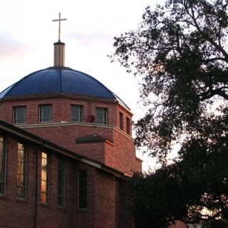 A brick church with a dome and cross, surrounded by trees at sunset.