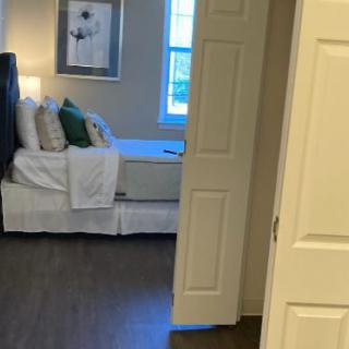 A cozy bedroom viewed through an open door, featuring a neatly made bed and decorative pillows.