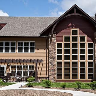 A modern residential building featuring a mix of wood and stone elements, with large windows that allow natural light to flood the interior.