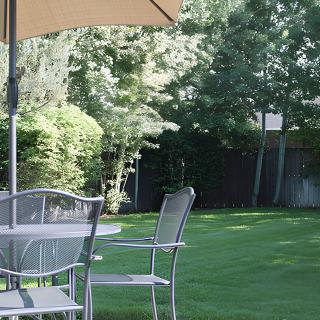 A peaceful garden setting with a patio table and chairs under a large umbrella, surrounded by greenery.