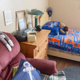 A cozy child's bedroom featuring a bed with blue-themed bedding, a stuffed animal, and a comfortable recliner.