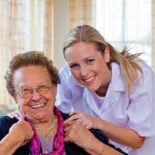A caregiver poses happily with an elderly woman, both smiling warmly.