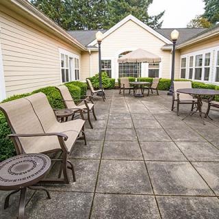 A spacious outdoor patio area with seating and tables, surrounded by a beige building and greenery.