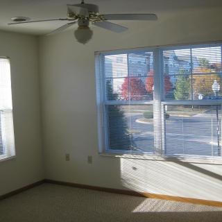 A bright, empty room with large windows and a ceiling fan.
