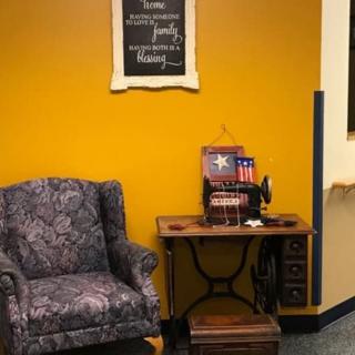 A cozy corner with a vintage armchair and sewing machine against a mustard yellow wall adorned with decor.