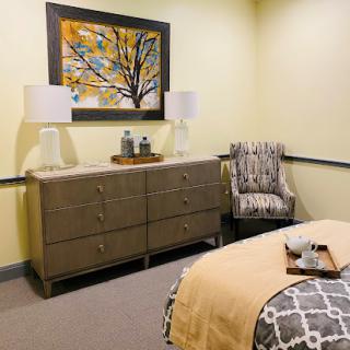 A cozy and elegantly decorated bedroom featuring a stylish dresser, modern lamps, and vibrant artwork.