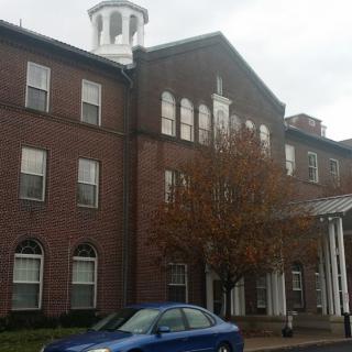A historic brick building with a cupola and parked blue car on an overcast day.