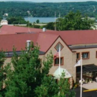 A building with a red roof surrounded by trees, overlooking a lake in the background.